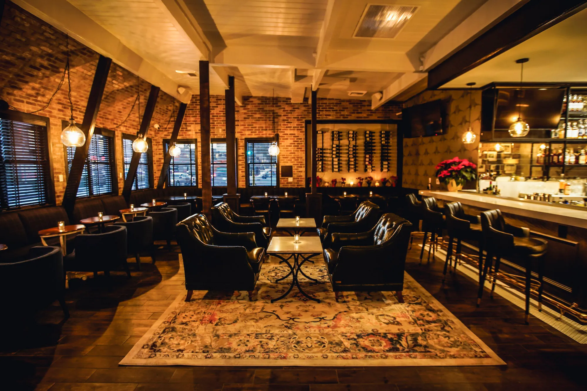 Warm, dimly lit bar interior with wood, metal back bar, and amber light over high tables.
